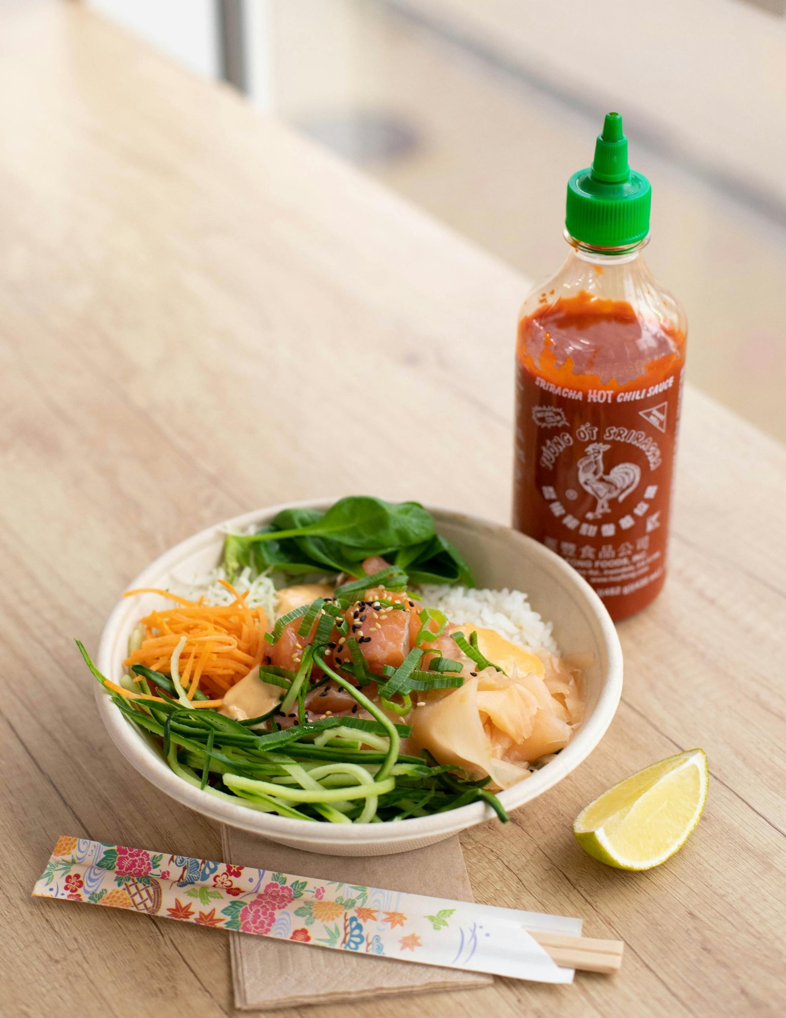 Delicious poké bowl topped with vegetables and served with Sriracha sauce.